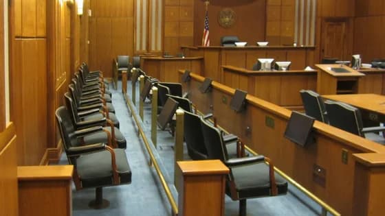 An empty courtroom with rows of jury chairs, the judge's bench, and a U.S. flag.