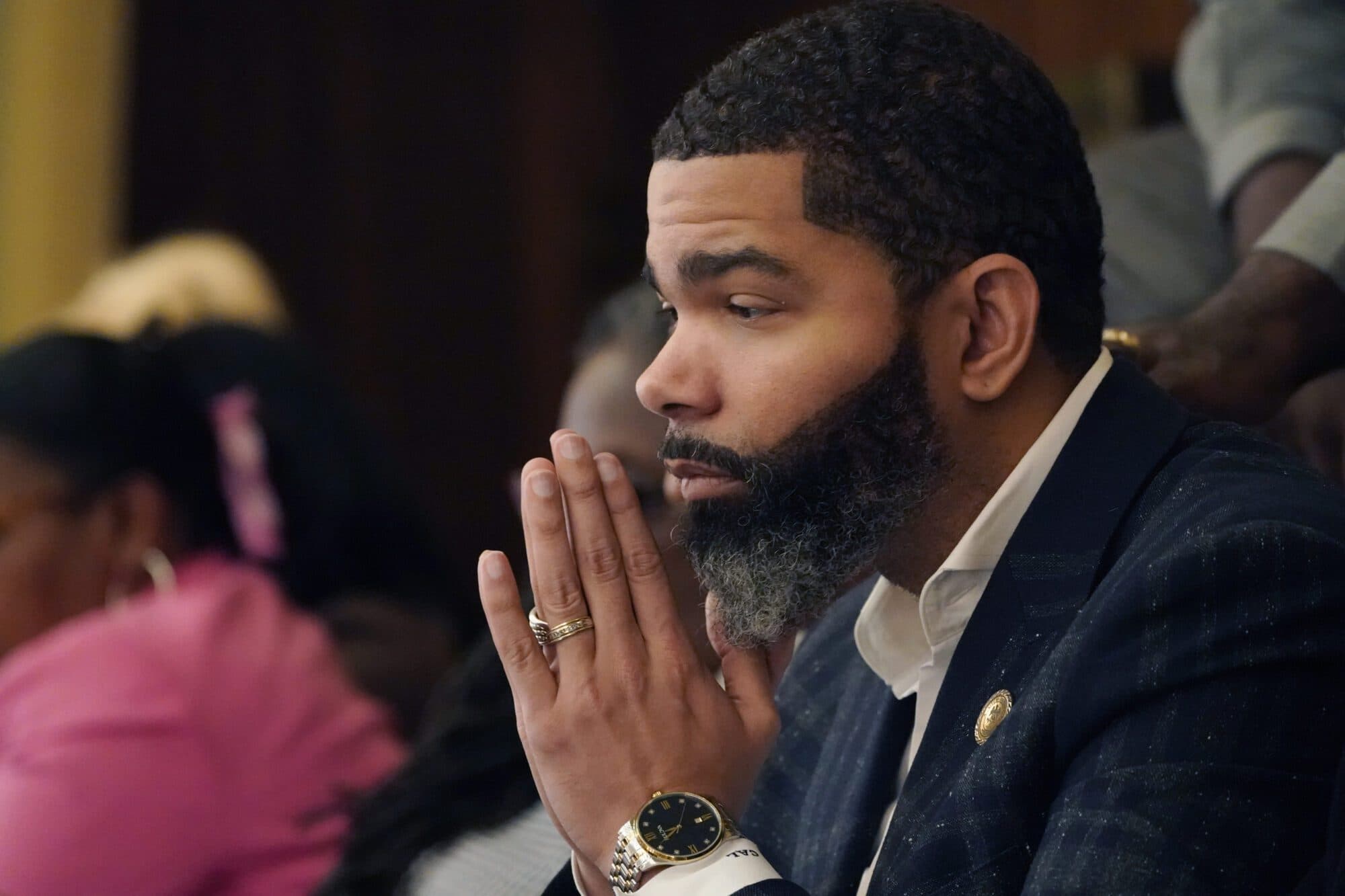 Former Jackson Mayor Chokwe Antar Lumumba, hands pressed together, listens during a public meeting.