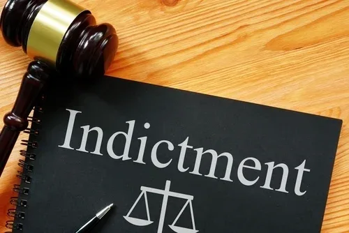 A black book titled “Indictment” next to a wooden judge's gavel on a desk.